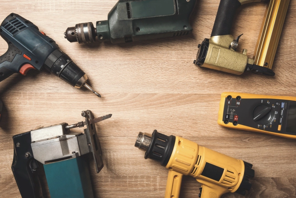 Ensemble d'outils de bricolage comprenant une perceuse, une scie sauteuse, un pistolet à clous et un multimètre, disposés sur une table en bois